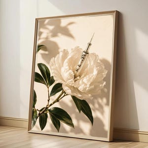 May include: A framed wall art print featuring a large, cream-coloured peony flower with a metallic medical syringe emerging from its centre. The botanical illustration includes dark green leaves and stems set against a light beige background.
