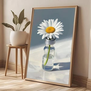 May include: A framed wall art print featuring a single white daisy with a yellow centre placed inside a clear glass medical vial. The vial has a silver cap and contains a green stem submerged in water, set against a soft blue and white background.