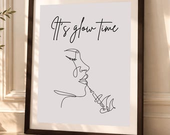 May include: A framed wall art print featuring a black continuous line drawing of a profile face holding a syringe near the lips, set against a light gray background. The text It's glow time is printed in black script above the illustration.