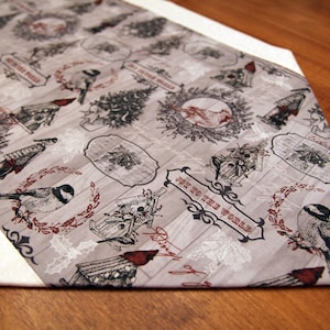 May include: A beige and white table runner with a repeating pattern of birds, houses, and trees. The text "Joy to the World" is printed in black on a white banner.