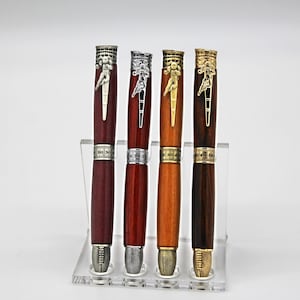 May include: Four wooden pens displayed in a clear acrylic stand. Each pen features a metallic clip shaped like a football player, a center band marked with yard line numbers 10, 20, 30, 40, and 50, and a tip designed to resemble a textured football.