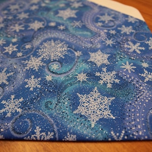 May include: Blue fabric with a white snowflake pattern. The fabric has a glittery finish and is ideal for crafting projects.
