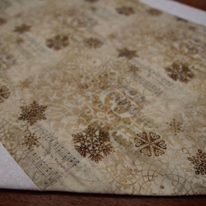 May include: A white table runner with a brown snowflake pattern and musical notes. The runner has a white border with a subtle glitter finish.