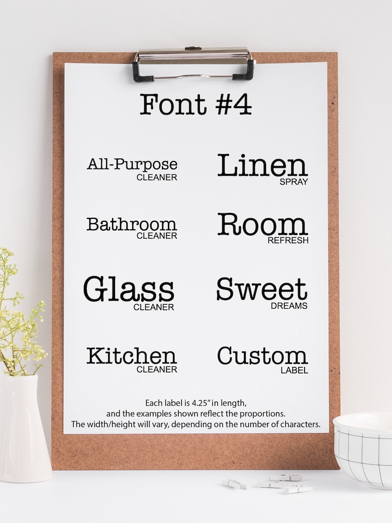 May include: A white sheet of paper with the text "Font #4" at the top. The paper is on a corkboard with a silver clip. The paper has examples of different font styles for labels, including "All-Purpose Cleaner", "Linen Spray", "Bathroom Cleaner", "Room Refresh", "Glass Cleaner", "Sweet Dreams", "Kitchen Cleaner", and "Custom Label". Each label is 4.25 inches long.