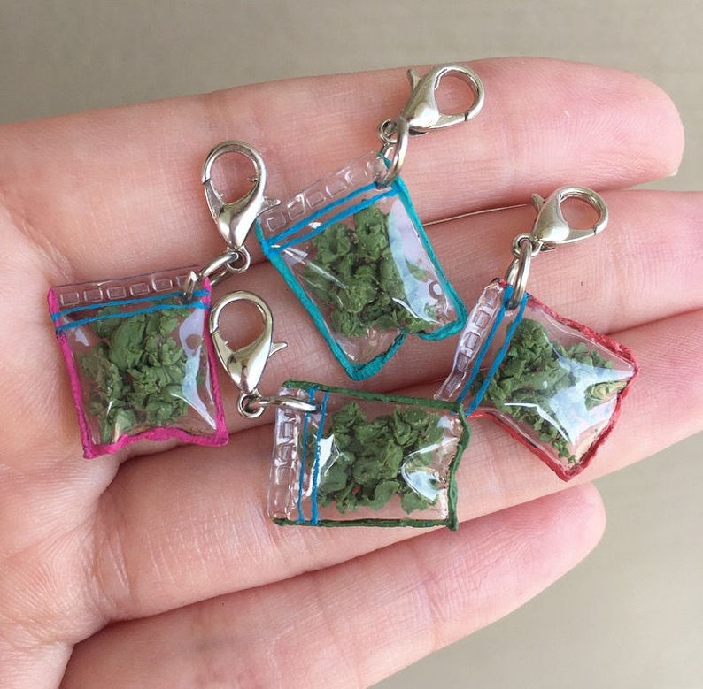 Puede incluir: Cuatro amuletos de bolsa de pl&aacute;stico transparente con cierres plateados. Cada bolsa contiene una sustancia verde frondosa y tiene un borde azul, rosa o turquesa.