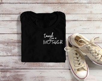 May include: Black t-shirt with the text "tough as a MOTHER" in white script. A pair of beige canvas sneakers with white laces are next to the shirt. The items are on a light wood-grain surface.