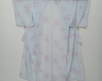 Puede incluir: Un kimono azul claro con un estampado floral rosa. El kimono está colgado en una percha sobre un fondo blanco.