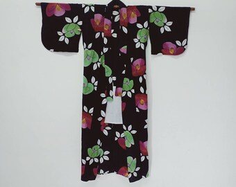Puede incluir: Un kimono negro con un patrón floral de flores rosas, rojas y verdes. El kimono tiene una faja blanca.