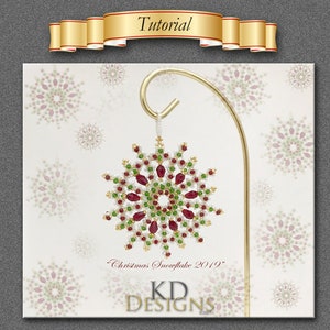 May include: A red, green, and white beaded snowflake ornament with a gold hanger. The ornament is labeled "Christmas Snowflake 2019" and "KD Designs".