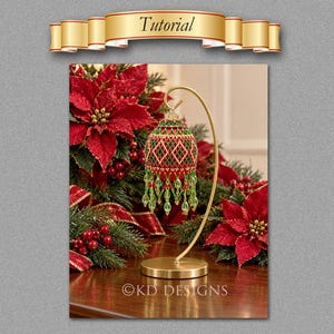 May include: A spherical ornament featuring a red and green beaded geometric pattern with dangling green crystal beads, suspended from a curved gold metal stand. The text "Tutorial" appears in a gold banner, and "KD DESIGNS" is at the bottom.