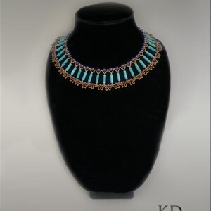 May include: A turquoise and purple beaded necklace with a gold-colored metal accent. The necklace is on a black display stand. "Summertime Fun" is written above the necklace.