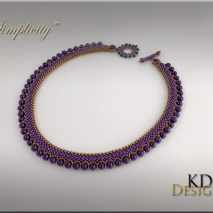 May include: A purple and gold beaded necklace with a toggle clasp. The necklace is called "Simplicity".