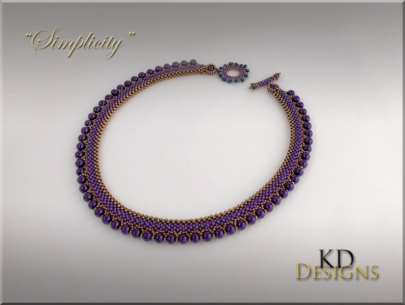 May include: A purple and gold beaded necklace with a toggle clasp. The necklace is called "Simplicity".
