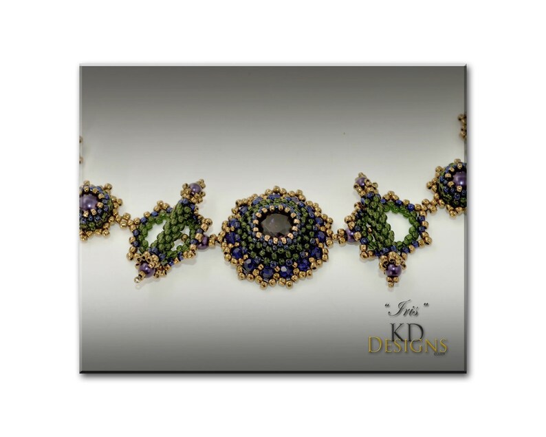 Puede incluir: Primer plano de un collar de cuentas con una piedra preciosa de color p&uacute;rpura oscuro en el centro. El collar est&aacute; hecho con cuentas verdes, doradas y moradas. El texto "Iris" y "KD Designs" es visible en la esquina inferior derecha de la imagen.
