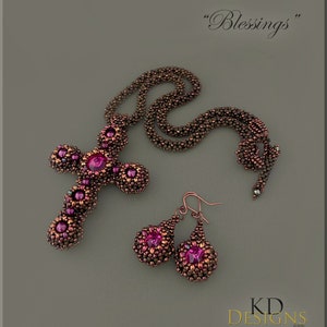 May include: A beaded cross necklace and earrings set with a pink gemstone in the centre of each piece. The necklace is made of brown and copper beads and the earrings are teardrop shaped. The set is labelled "Blessings".