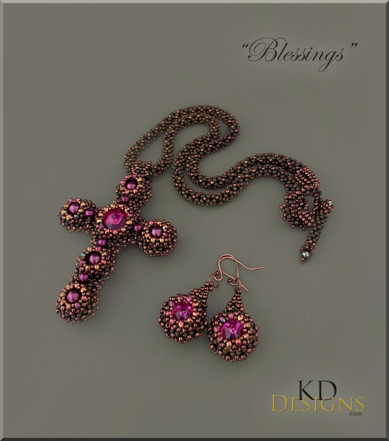 May include: A beaded cross necklace and earrings set with a pink gemstone in the centre of each piece. The necklace is made of brown and copper beads and the earrings are teardrop shaped. The set is labelled "Blessings".