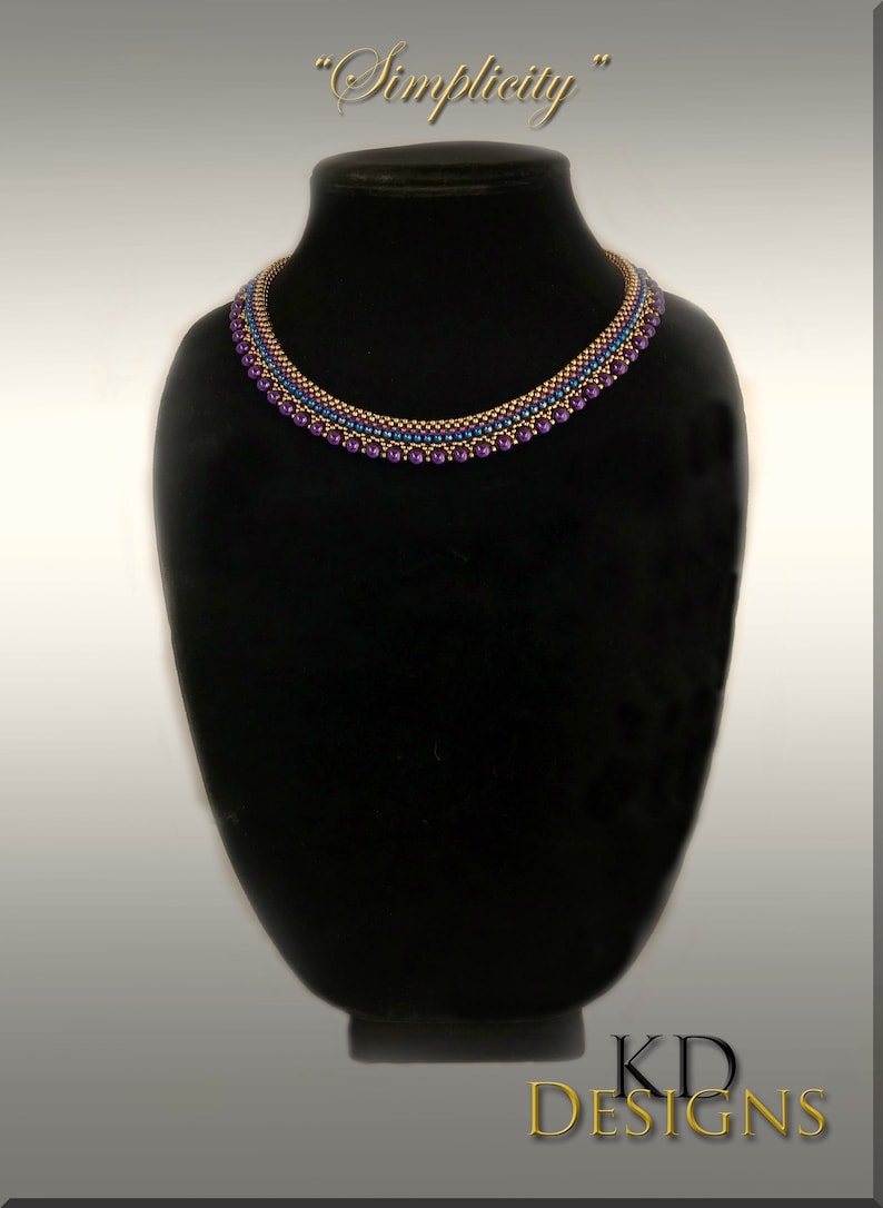 May include: A gold and purple beaded necklace on a black display stand. The necklace has a simple design and is labeled "Simplicity".