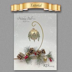 May include: A gold beaded bauble with green accents hangs from a stand. The bauble is decorated with a small gold star and has a beaded fringe. The bauble is surrounded by pine branches and pine cones.