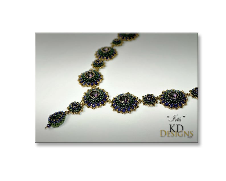 Puede incluir: Un collar de cuentas con un esquema de color verde, azul y dorado. El collar presenta una serie de medallones redondos de cuentas con una piedra preciosa p&uacute;rpura central. El collar est&aacute; etiquetado como "Iris" KD Designs.