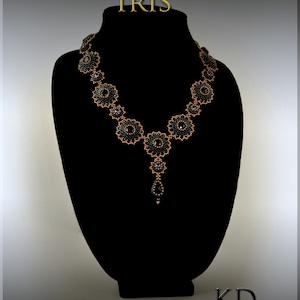 Puede incluir: Un collar de cuentas negras con un acento dorado, que presenta un dise&ntilde;o floral. El collar se muestra en un busto de maniqu&iacute; negro. El texto "IRIS" se muestra sobre el collar. El texto "KD DESIGNS" se muestra debajo del collar.