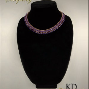 May include: A purple and copper beaded necklace on a black mannequin. The necklace is made with small beads and has a simple design. The text "Simplicity" is written above the necklace.