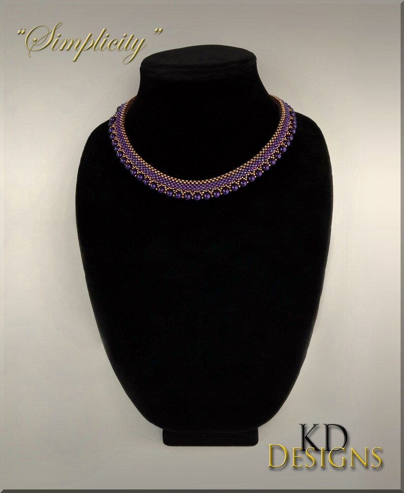May include: A purple and copper beaded necklace on a black mannequin. The necklace is made with small beads and has a simple design. The text "Simplicity" is written above the necklace.