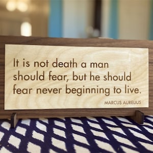 May include: A wooden sign with a quote by Marcus Aurelius: "It is not death a man should fear, but he should fear never beginning to live."