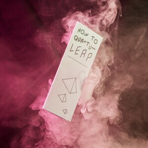 May include: A white pamphlet with the text "HOW TO QUANTUM LEAP" and a series of triangles on the bottom. The pamphlet is floating in a cloud of pink and white smoke.