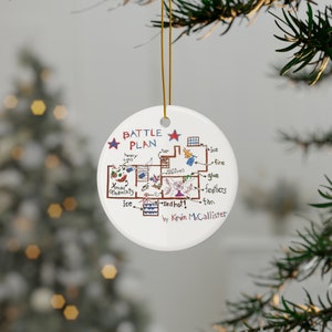 May include: A white ceramic Christmas ornament with a hand-drawn map of a house. The map is titled "Battle Plan" and includes details like "ice", "fire", "glue", and "feathers". The map is signed "by Kevin McCallister".