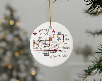 May include: A white ceramic Christmas bauble featuring a hand-drawn map of a house. The map is titled "Battle Plan" and includes details such as "ice", "fire", "glue", and "feathers". The map is signed "by Kevin McCallister".