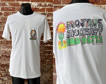 May include: White t-shirt with a graphic print on the back that says "Mojave Mo Heavy Mo Betta". The graphic is in a colorful, cartoon style with a sun, cactus, and mountains.