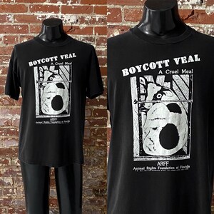 May include: Black t-shirt with a white graphic of a calf in a crate. The graphic says "Boycott Veal, A Cruel Meal" and "ARFF, Animal Rights Foundation of Florida".