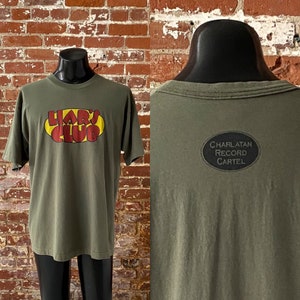 90er Jahre Liar's Club Band Promo T-Shirt. Vintage Anfang der 1990er Jahre Liar's Club Scharlatan Plattenkartell-Label-T-Shirt. Einzelstich - Groß / XL 23 "x 31"