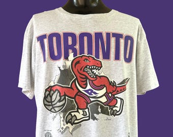 Camiseta gráfica de baloncesto de la NBA de los Toronto Raptors de 1994 con estampado a doble cara "Bustin' Thru". Fabricada en EE. UU. Talla XL (23,5" x 30,75").