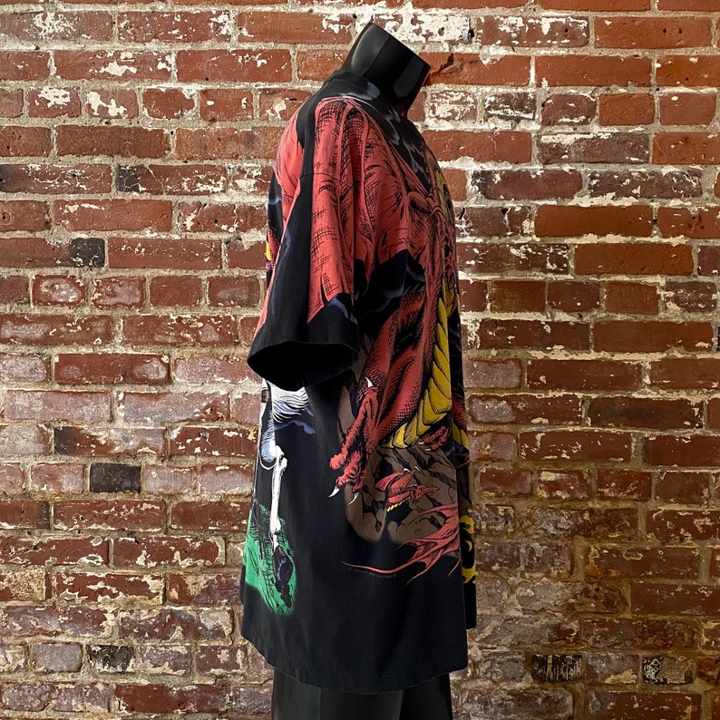 Może przedstawiać: Czarna koszula w stylu kimono z żywą ilustracją smoka w kolorze czerwonym, ż&oacute;łtym i brązowym. Koszula ma kr&oacute;tkie rękawy i luźny kr&oacute;j. Wz&oacute;r smoka pokrywa prz&oacute;d i tył koszuli.