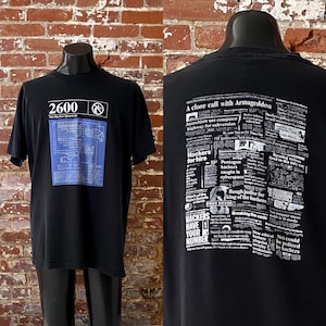 May include: Black t-shirt with a blue and white graphic of a computer circuit board and the text "2600 The Hacker Quarterly". The back of the shirt features a black and white newspaper print design with the text "A close call with Armageddon" and "Hackers for hire".