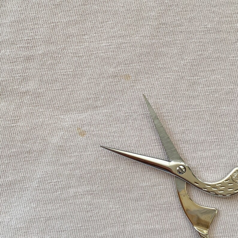 May include: A pair of silver-colored scissors with a bird-shaped handle. The scissors are on a white fabric background.