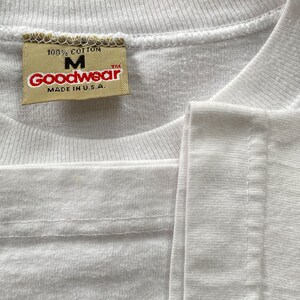 May include: White t-shirt with a yellow tag that reads "100% Cotton, M, Goodwear, TM, Made in U.S.A."