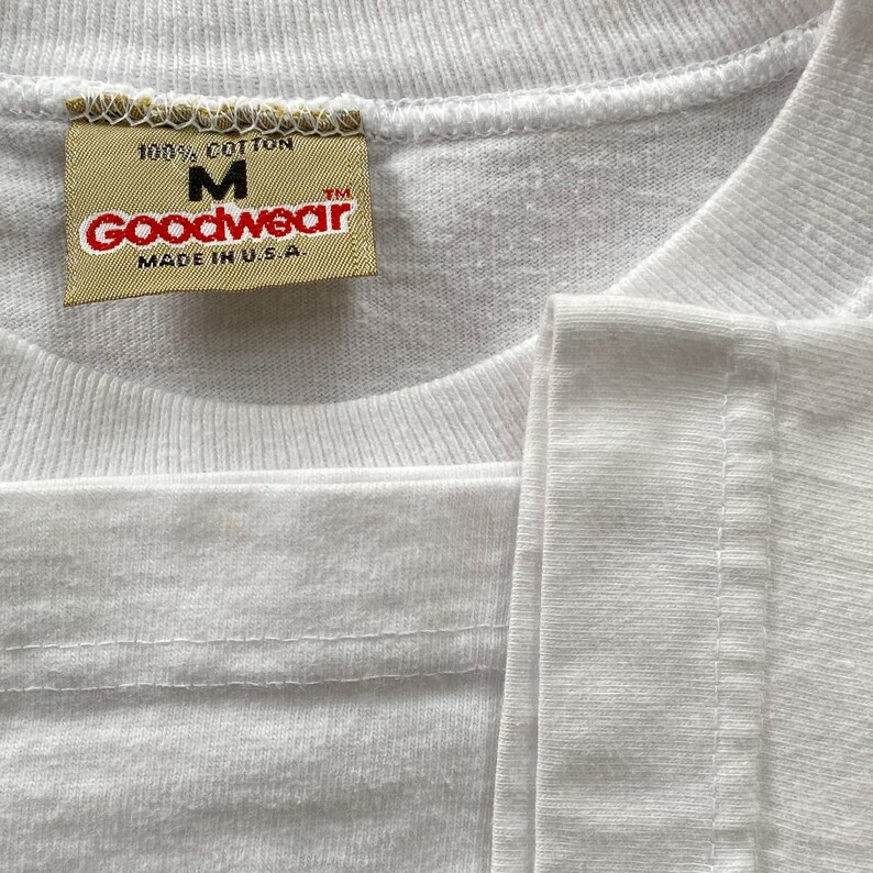 May include: White t-shirt with a yellow tag that reads "100% Cotton, M, Goodwear, TM, Made in U.S.A."