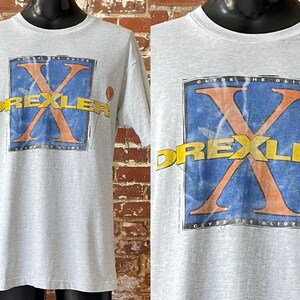 May include: Grey t-shirt with a vintage graphic print of Clyde the Glide, featuring a large orange X with the text "Drexler" in yellow letters.