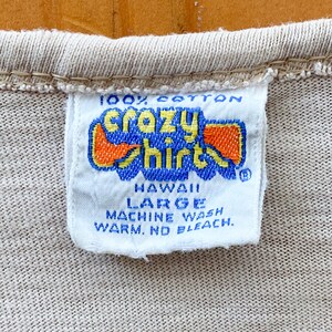 May include: White tag with blue and orange text that reads "100% cotton Crazy Shirts Hawaii Large Machine Wash Warm. No Bleach."