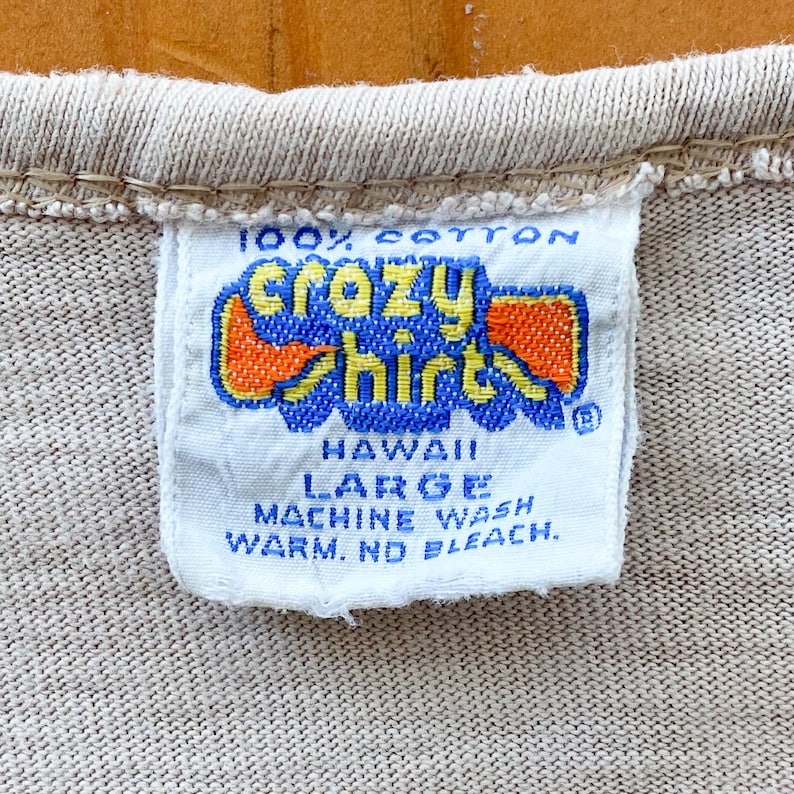 May include: White tag with blue and orange text that reads "100% cotton Crazy Shirts Hawaii Large Machine Wash Warm. No Bleach."