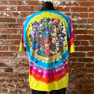 Op de afbeelding: Tie-dye T-shirt met een kleurrijke afbeelding van cartoonberen die muziek maken. De tekst "Grateful Dead" en "River Jamboree" staat op het shirt gedrukt.