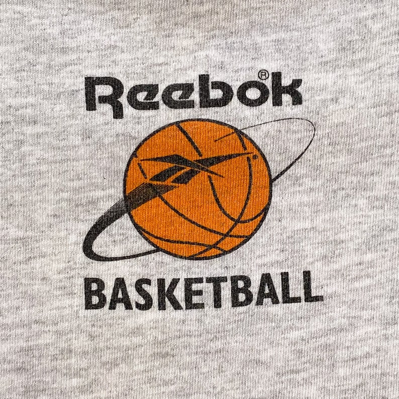 May include: A gray sweatshirt with the Reebok logo and the words "Basketball" printed on it. A basketball with an orange and black design is in the center of the sweatshirt.
