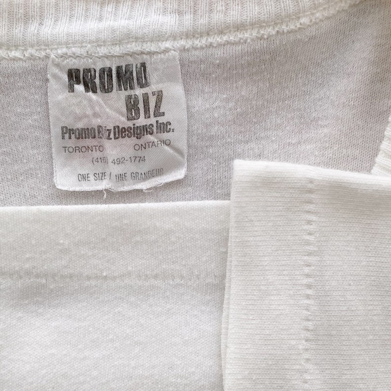 May include: White tag with black text that reads "PROMO BIZ Promo Biz Designs Inc. TORONTO ONTARIO (415) 492-1774 ONE SIZE/UNE GRANDEUR"