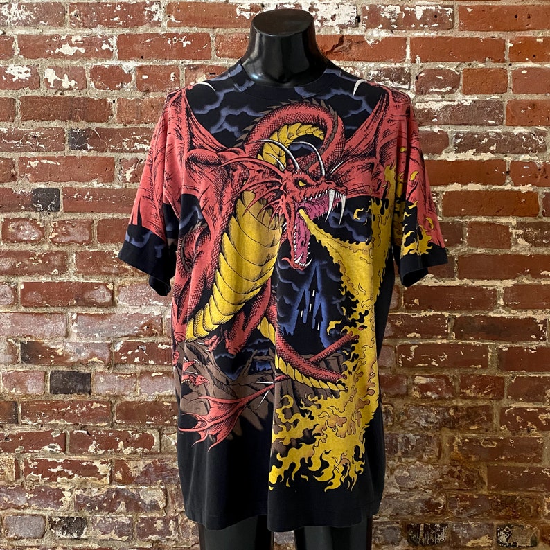 Może przedstawiać: Czarny t-shirt z efektownym wzorem czerwonego i ż&oacute;łtego smoka ziejącego ogniem. Grafika smoka jest nadrukowana na przodzie i rękawach. Koszulka jest prezentowana na czarnym manekinie.