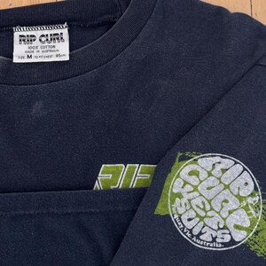 May include: Navy blue long-sleeve shirt with the text "RIP CURL" in white and green. The shirt has a crew neck and a graphic on the sleeve that says "RIP CURL" in a circular design. The shirt is size M, fits a 95cm chest, and is made of 100% cotton.