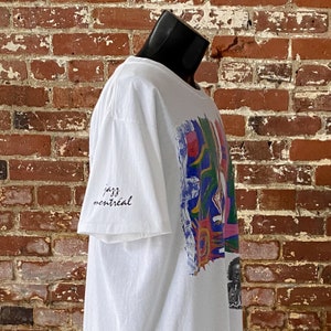 May include: White t-shirt with a colorful abstract design and the text "jazz montreal" on the sleeve.