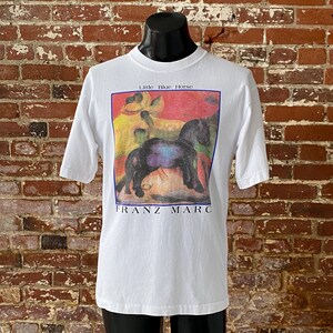 May include: White t-shirt with a colorful image of a black horse and the text "Little Blue Horse" and "FRANZ MARC" printed on the front.