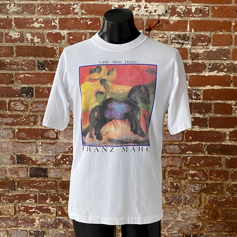 May include: White t-shirt with a colorful image of a black horse and the text "Little Blue Horse" and "FRANZ MARC" printed on the front.